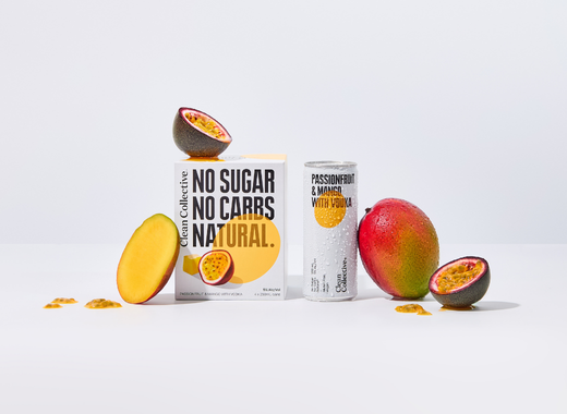 A white can of Clean Collective Passionfruit & Mango premixed drink with 'No Sugar, No Carbs, Natural' printed on it, displayed alongside fresh cut mango slices and passionfruit halves.