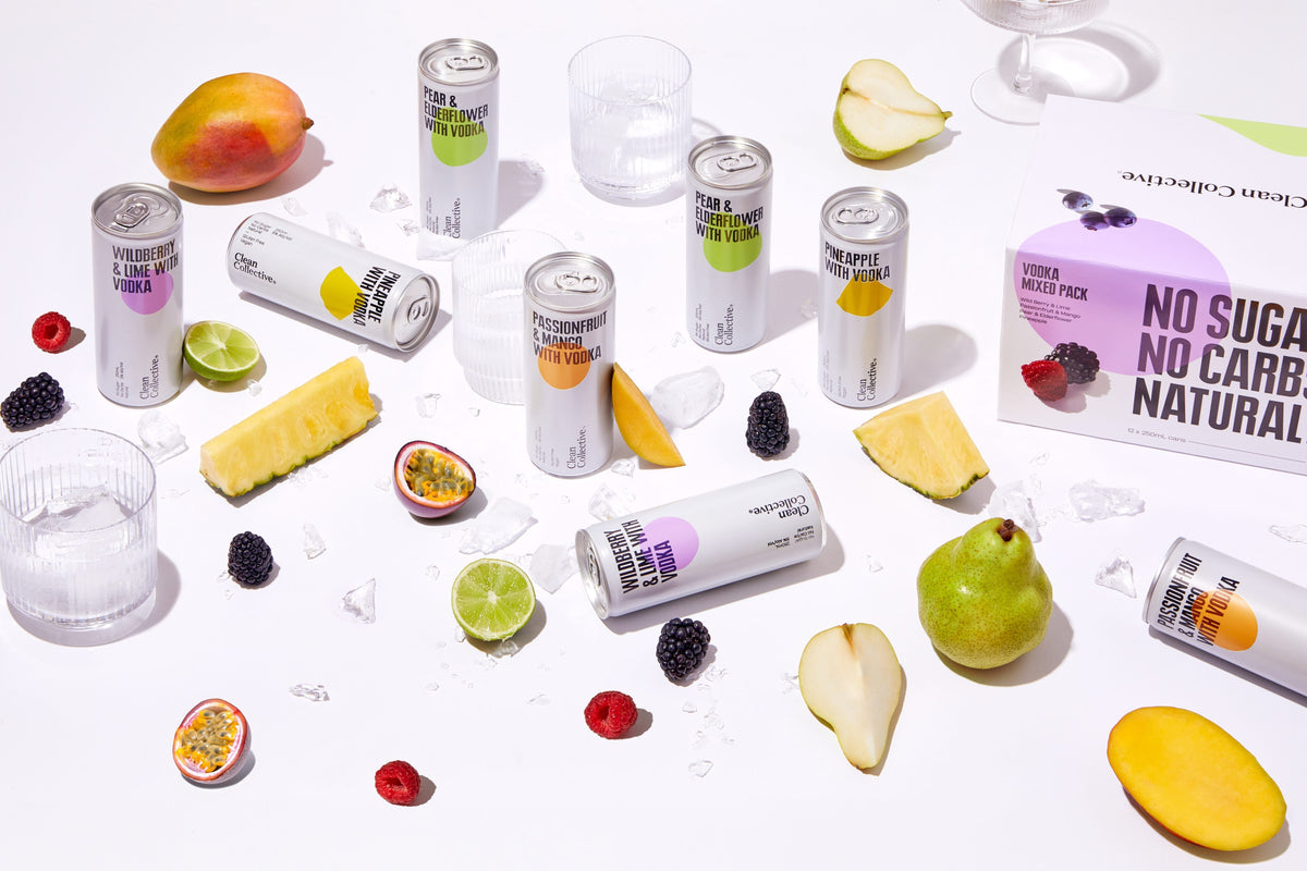 A vibrant flat-lay of Clean Collective canned energy drinks scattered among fresh sliced fruits and ingredients on a white background.