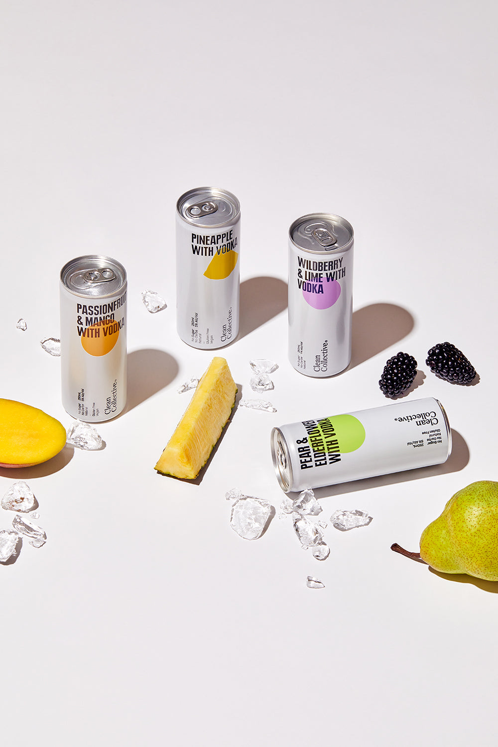 A selection of Clean Collective canned premixed alcoholic drinks displayed alongside fresh sliced fruit, including citrus and pears, on a minimal white surface.