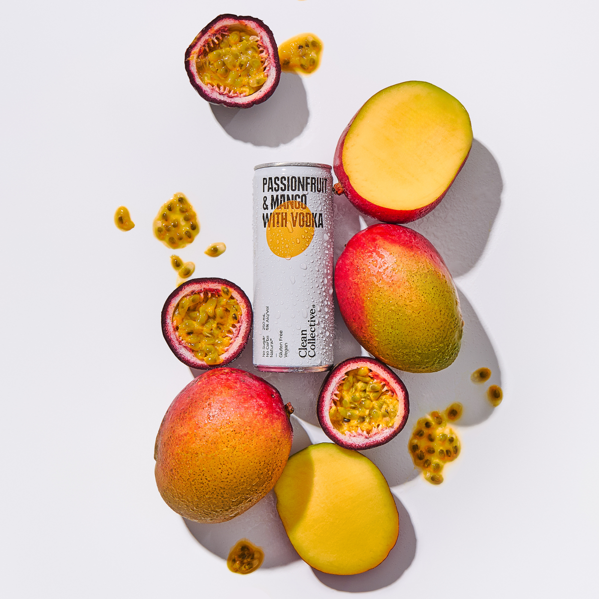 A can of Clean Collective Passionfruit & Mango energy drink resting on a white surface, surrounded by fresh halved passion fruits and sliced ripe mangoes.